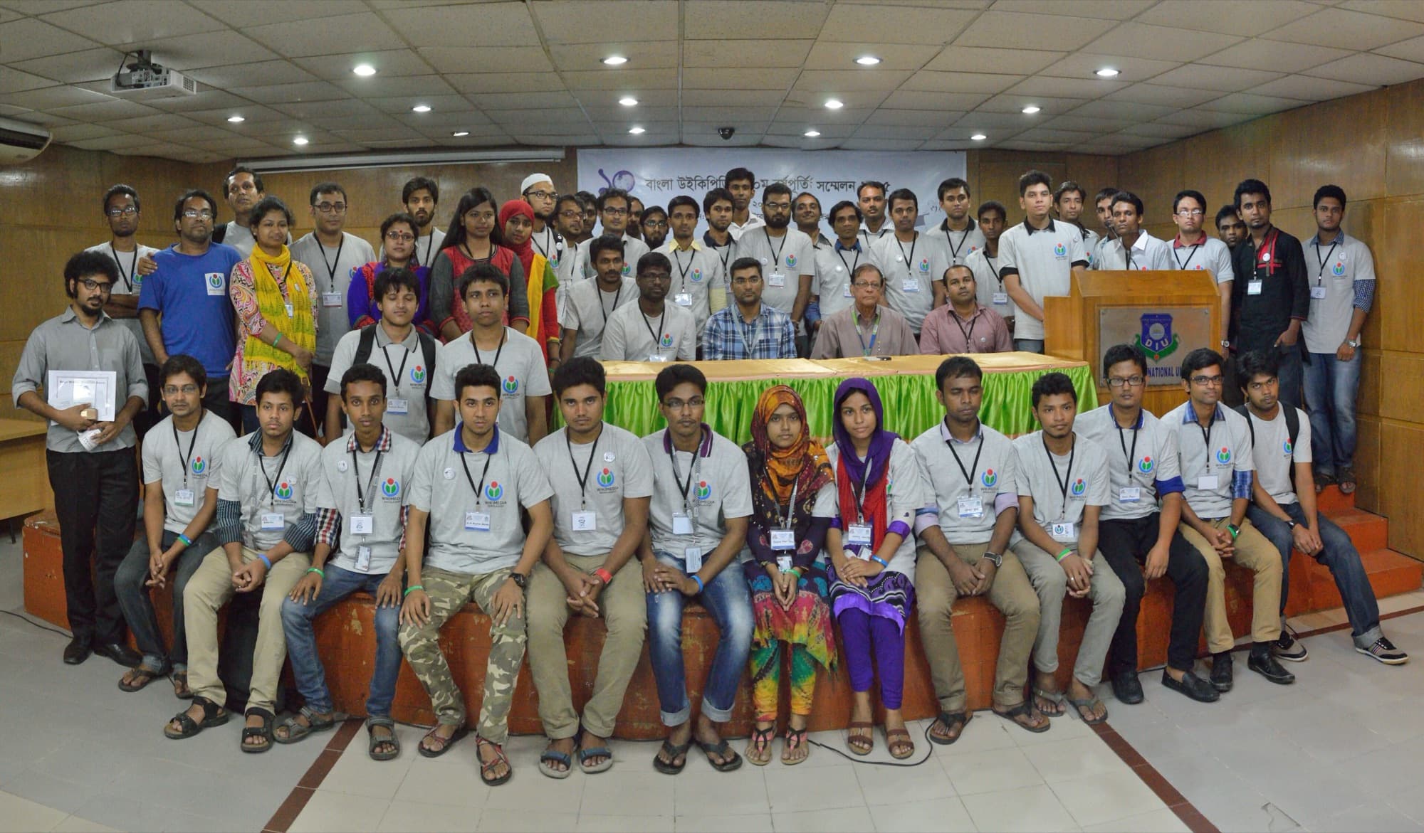 A large group photographed together in a university hall in Dhaka