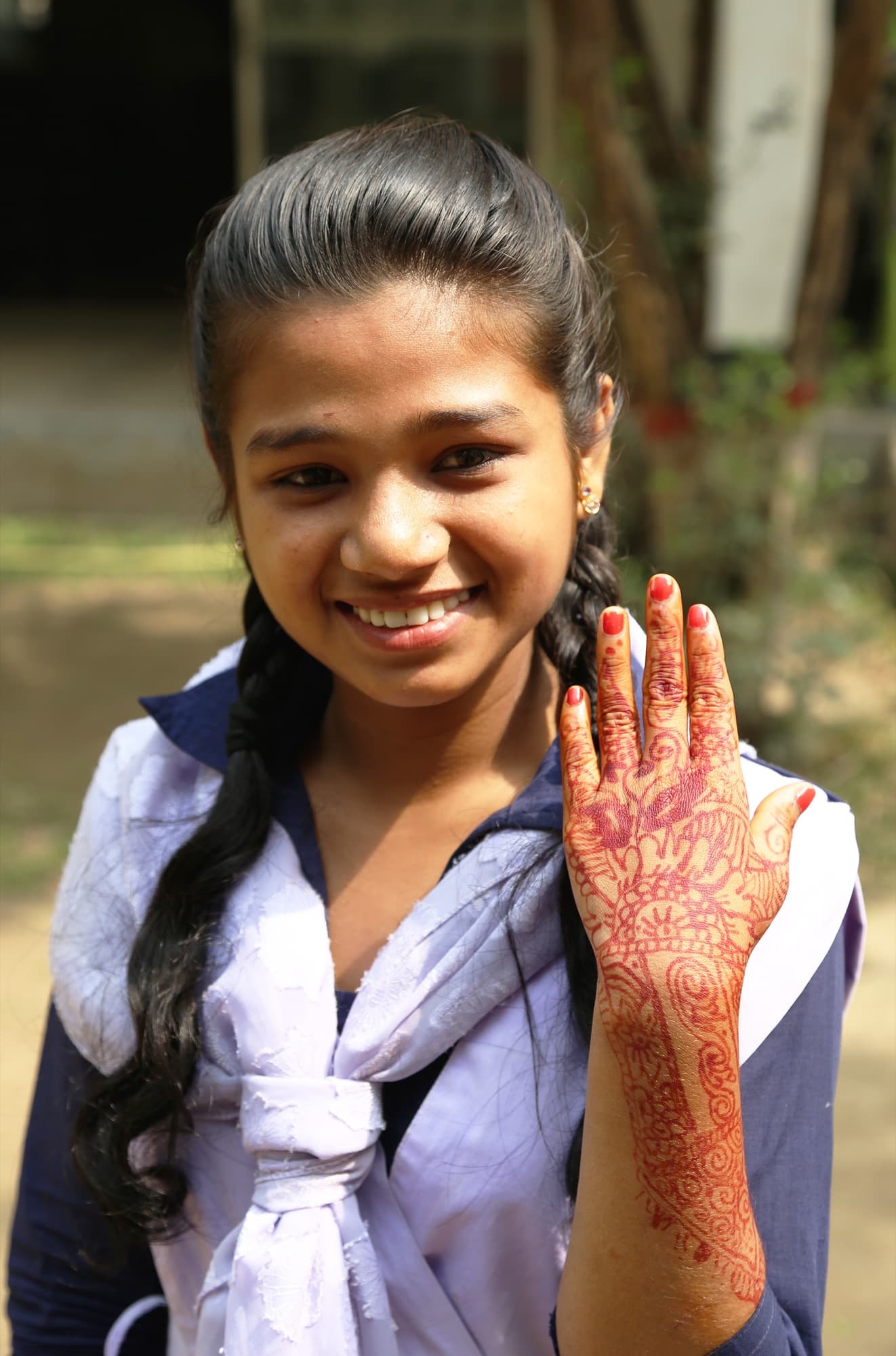 A schoolgirl smiling and holding up a hand painted with henna
